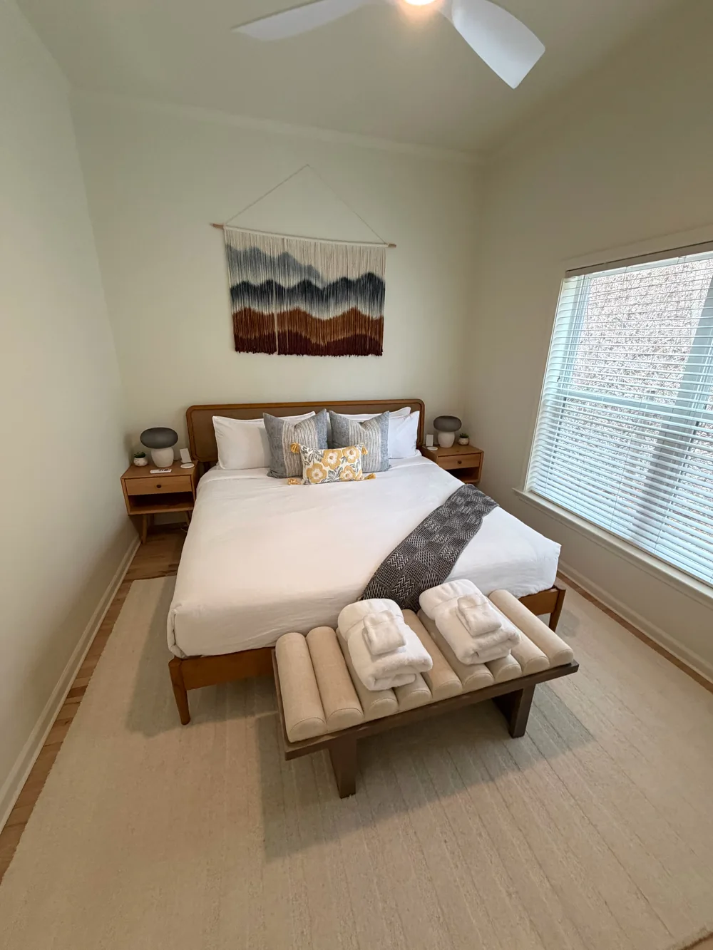 A bright bedroom with a made bed and folded towels arranged on a wood bench.