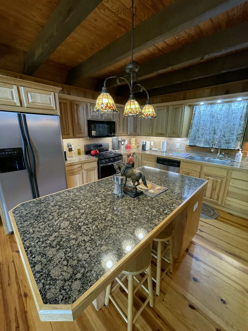 Cabin kitchen with granite island, pendant lights, and exposed beams