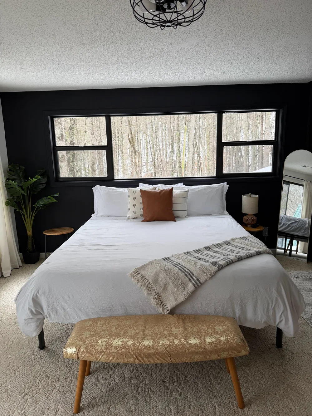 A made bed with white linens, a patterned throw, and a bench against a dark accent wall.