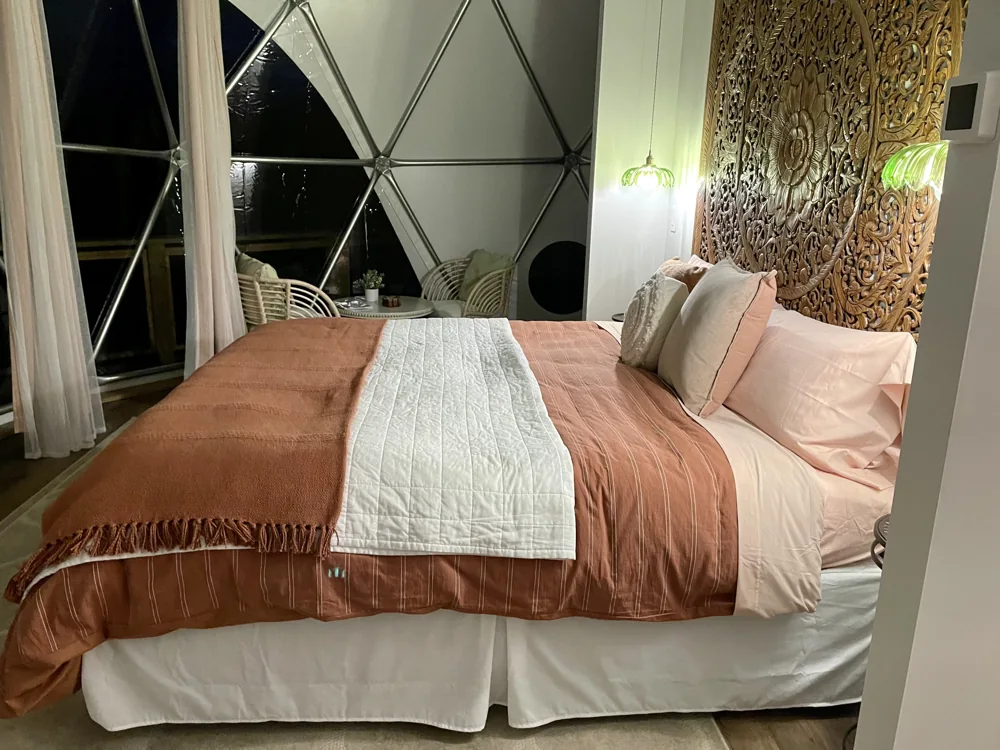 Dome bedroom with terracotta bedding, a gold headboard, and geometric windows