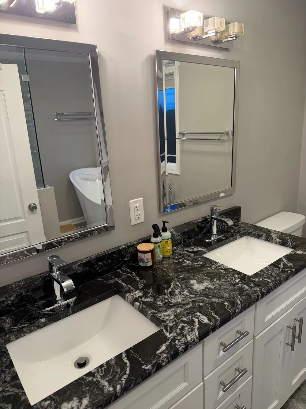 A double vanity with white sinks, dark stone counters, and two mirrors.