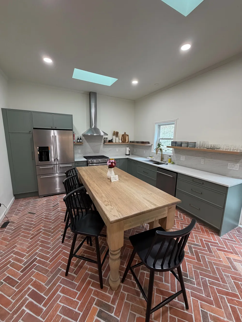 A green kitchen with a wood island, brick flooring, and light from above.