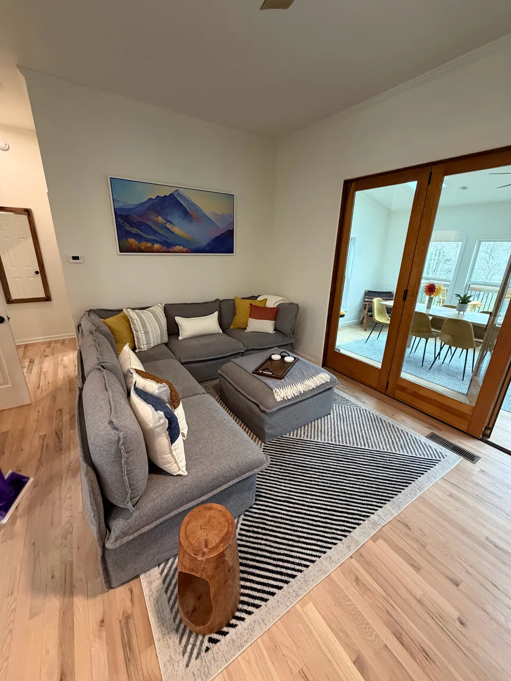 A gray sectional with arranged cushions, a striped rug, and glass doors to the next room.