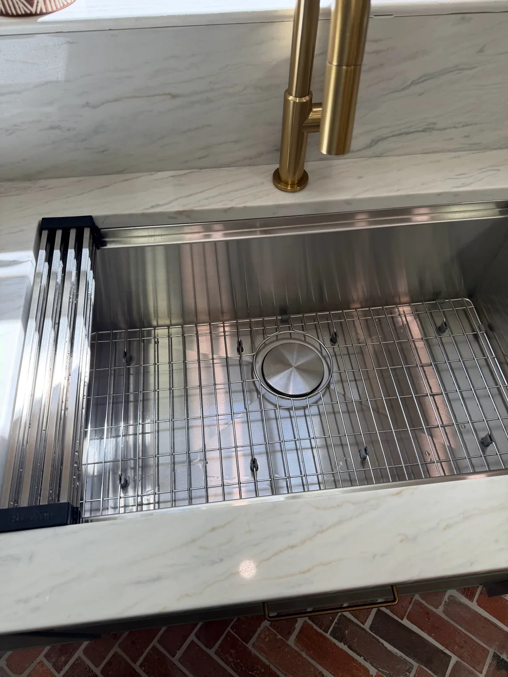 A stainless steel sink with a fitted rack and a gold-tone faucet.
