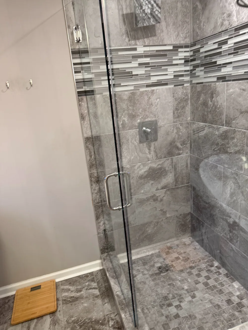 A glass shower enclosure with gray tile and a mosaic accent.