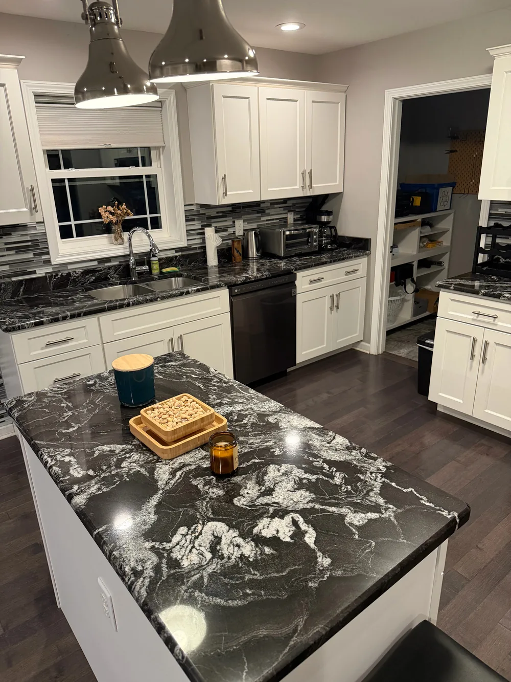 White cabinets and dark patterned stone counters around a kitchen island.
